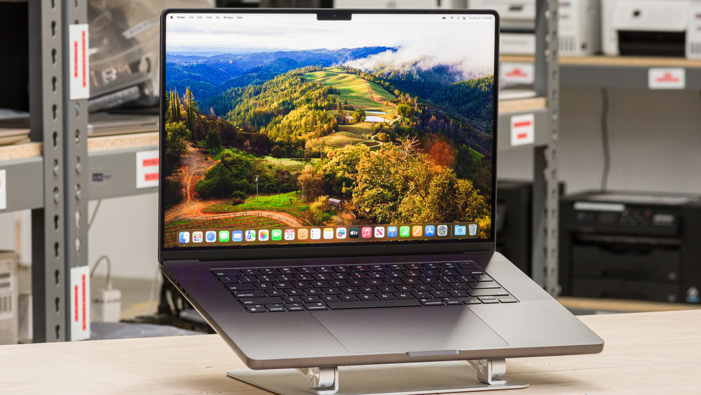 Apple MacBook Pro 16 M3 Pro laptop on a stand, displaying a vibrant macOS desktop with a scenic landscape.