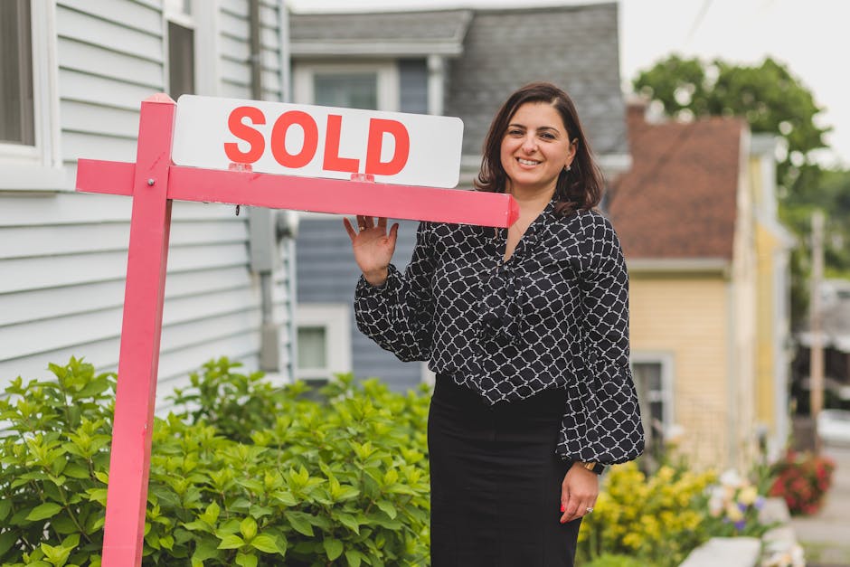 Smiling female real estate agent holds a 'SOLD' sign in a residential neighborhood, signifying a successful property sale.
