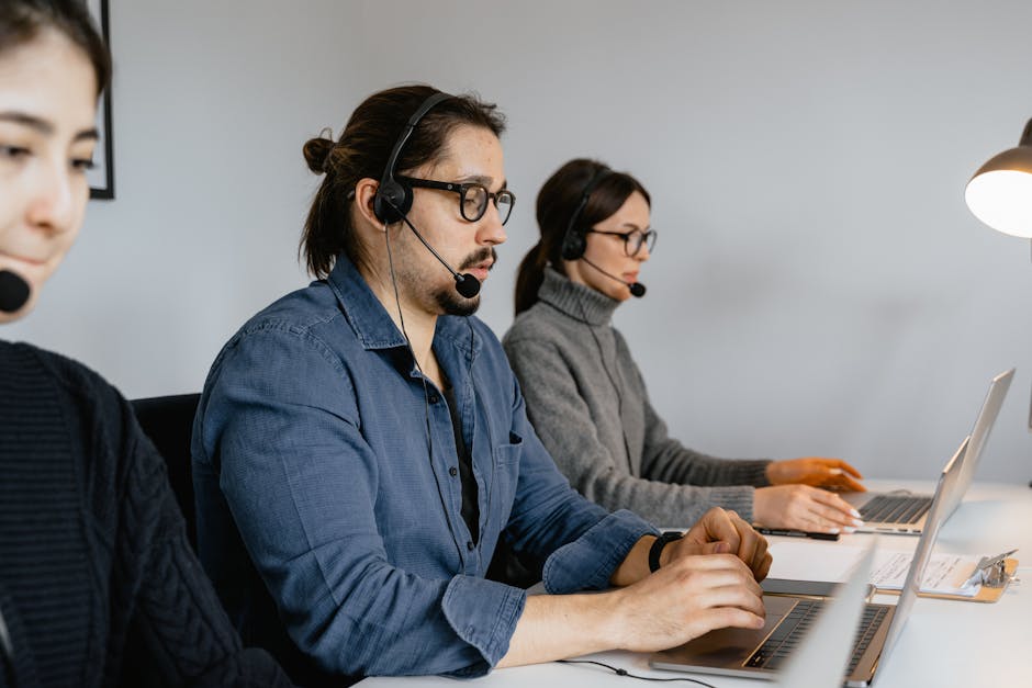 Three customer support agents with headsets and laptops working at desks, representing online assistance.