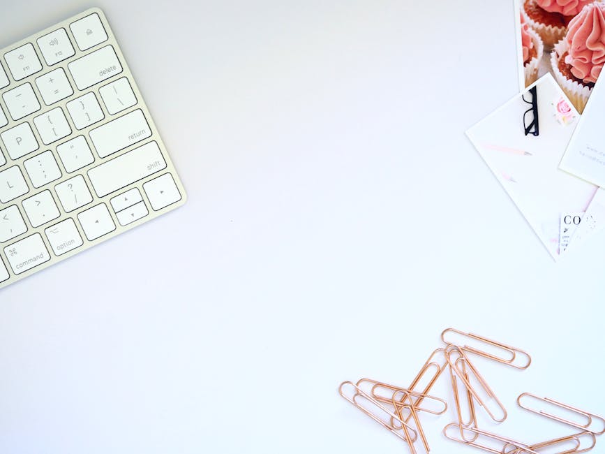 Clean white desk with a computer keyboard, documents, and rose gold paper clips for digital content creation.