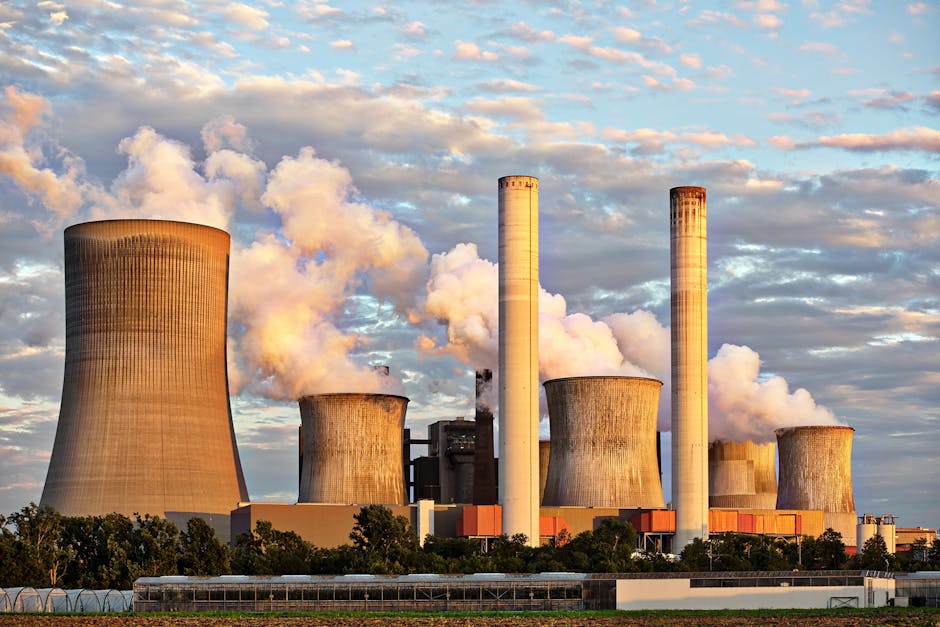 Large industrial power plant with multiple cooling towers and smokestacks emitting steam, highlighting infrastructure and resource management.