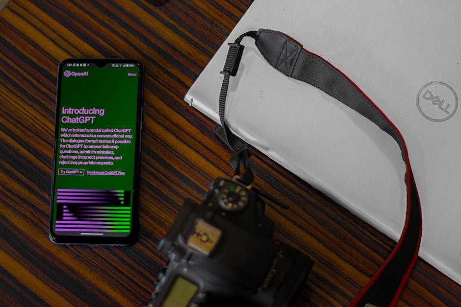 Smartphone displays OpenAI ChatGPT introduction, symbolizing AI text generation, on a desk with a laptop and camera.