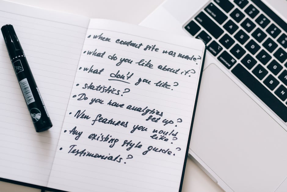 Open notebook with handwritten questions for website content strategy, a black pen, and a laptop keyboard.