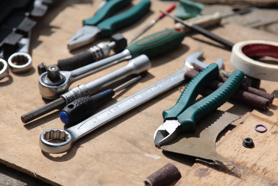 Various hand tools including wrenches, pliers, screwdrivers, sockets, and tape laid out on a wooden surface.